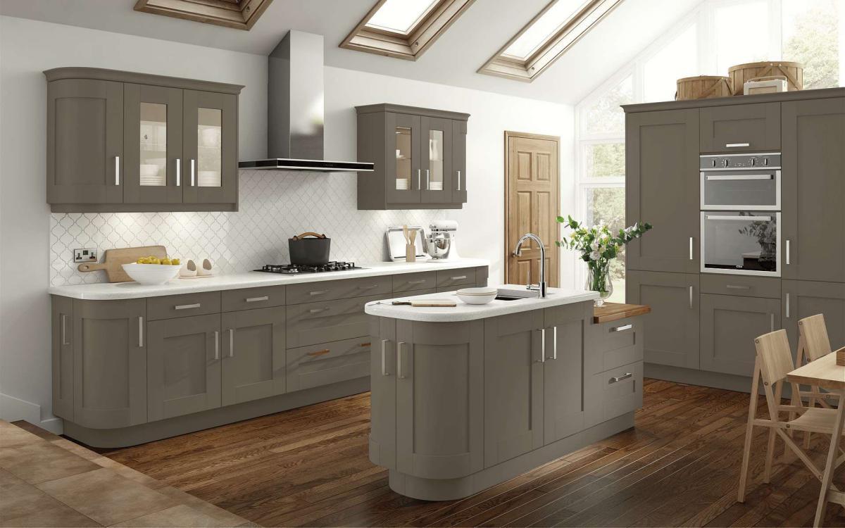 Kitchen with radius end to the island, glass wall units, and three tall units housing a double oven in Bowood Stone Grey style